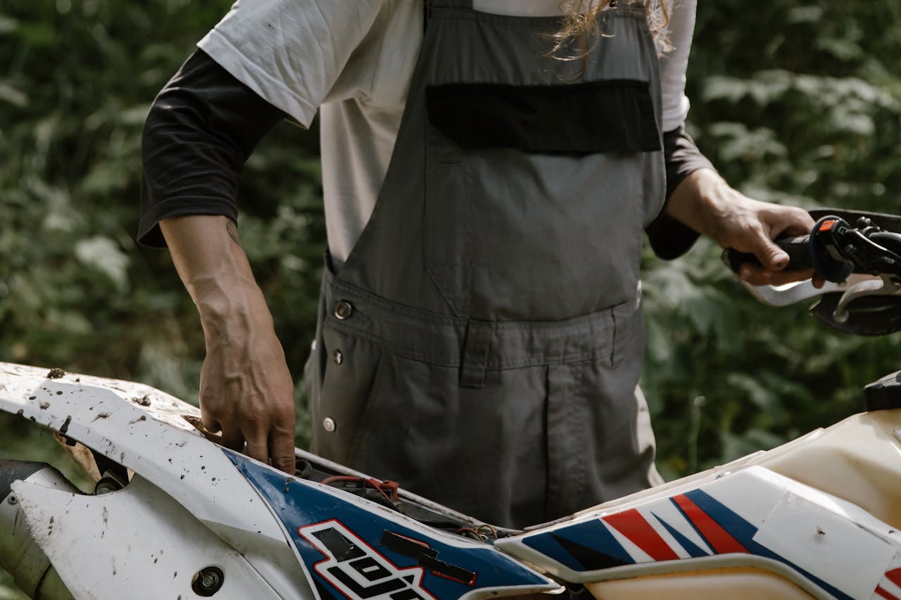 Close-up of a mechanic fixing an off-road motorcycle in an outdoor setting. Perfect for adventure and lifestyle themes.